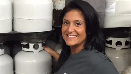 Portrait of a woman with t-shirt standing in front of several white LPG cylinders on shelfs CNB