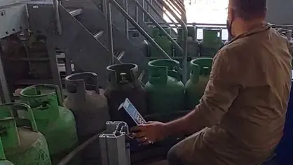image of a worker using a crisplant universal controller and handling green lpg cylinders on a conveyor chain